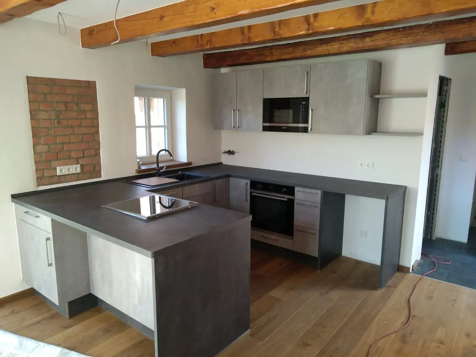 Moderne Küche mit grauen Schränken, Holzdecke und Arbeitsplatten aus Stein.