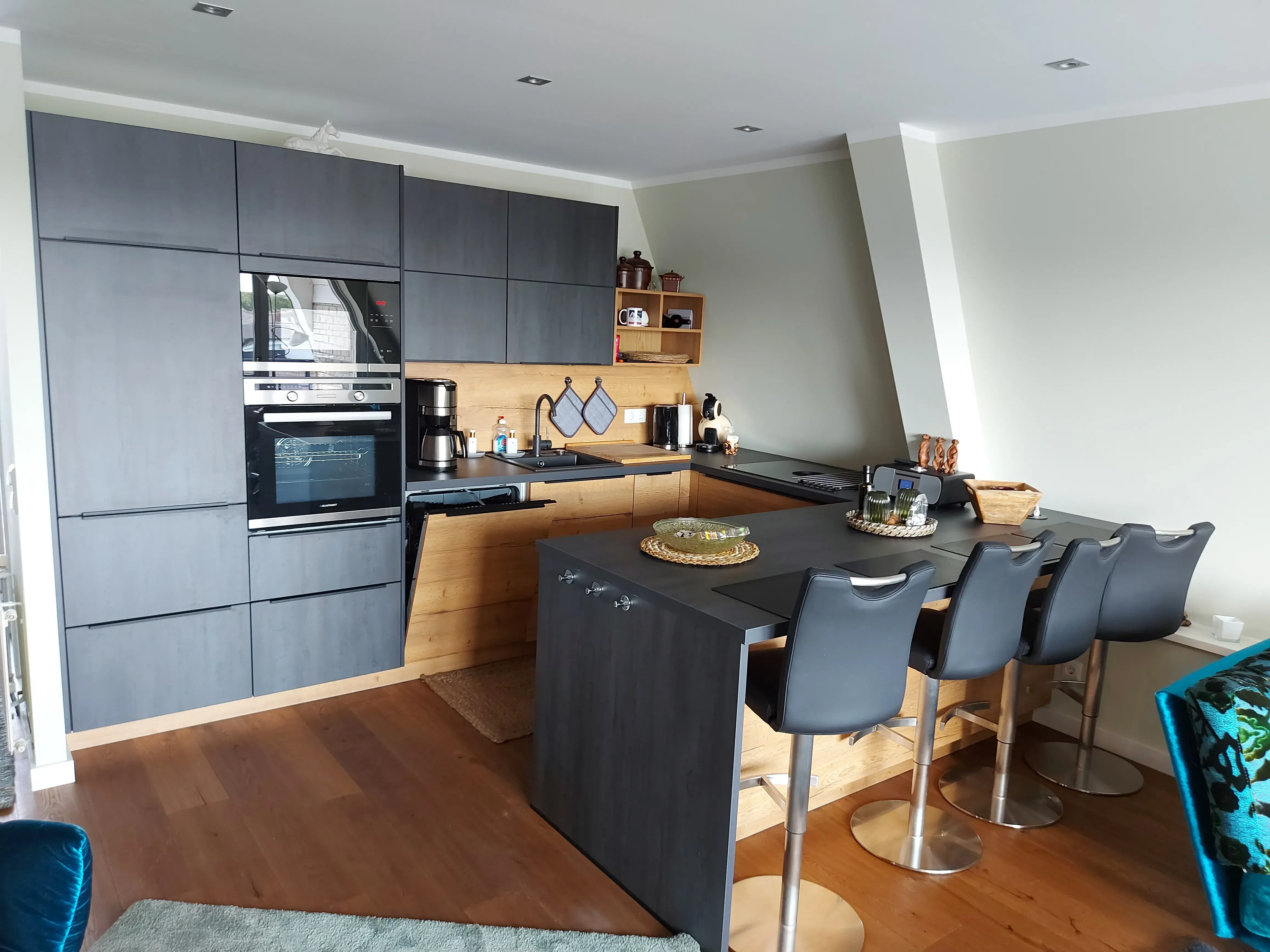 Moderne Küche mit grauen Schränken, Holzboden und vier Barhockern an der Theke.