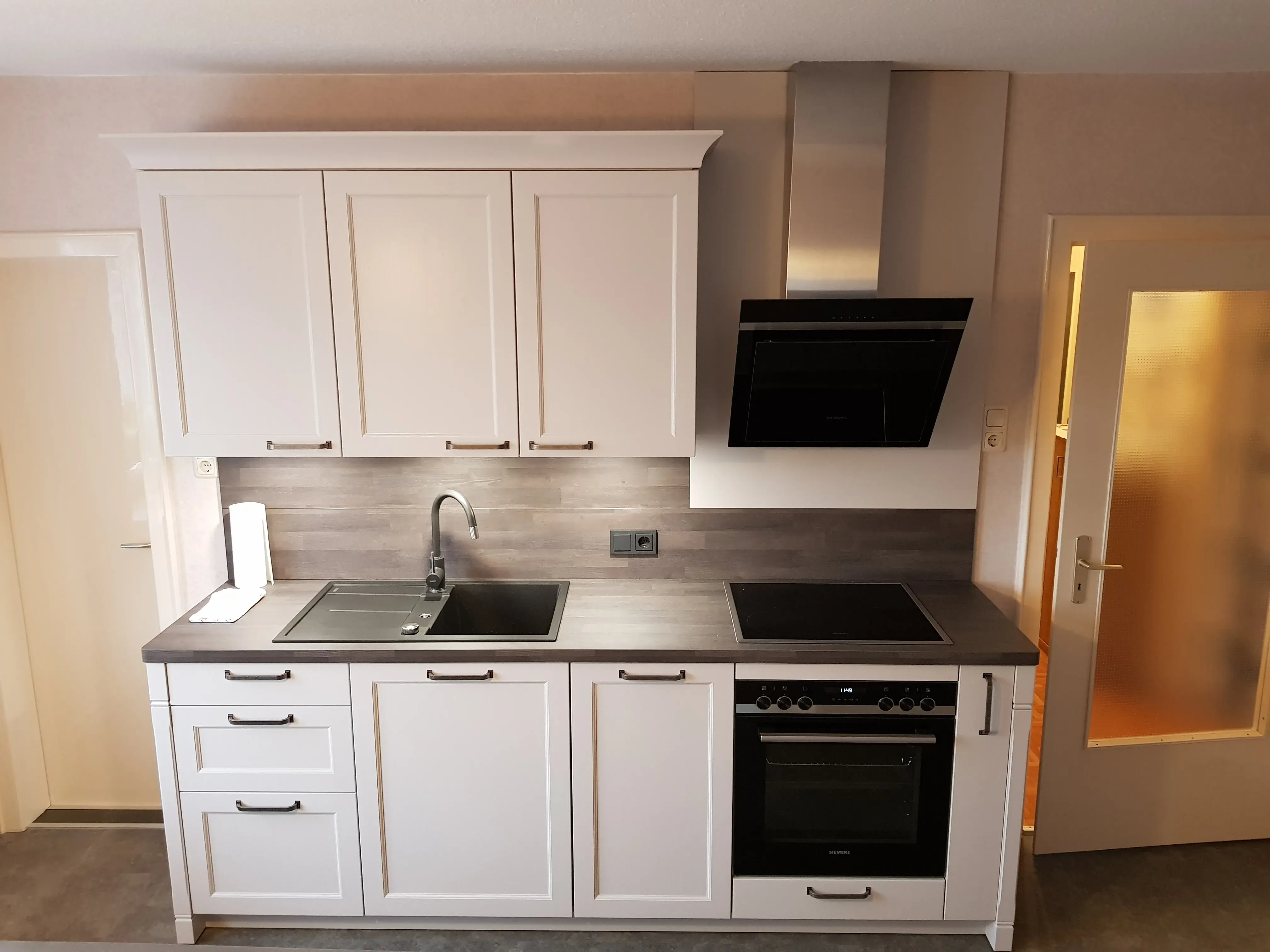 Moderne weiße Einbauküche mit Herd, Spüle und grauer Arbeitsplatte.