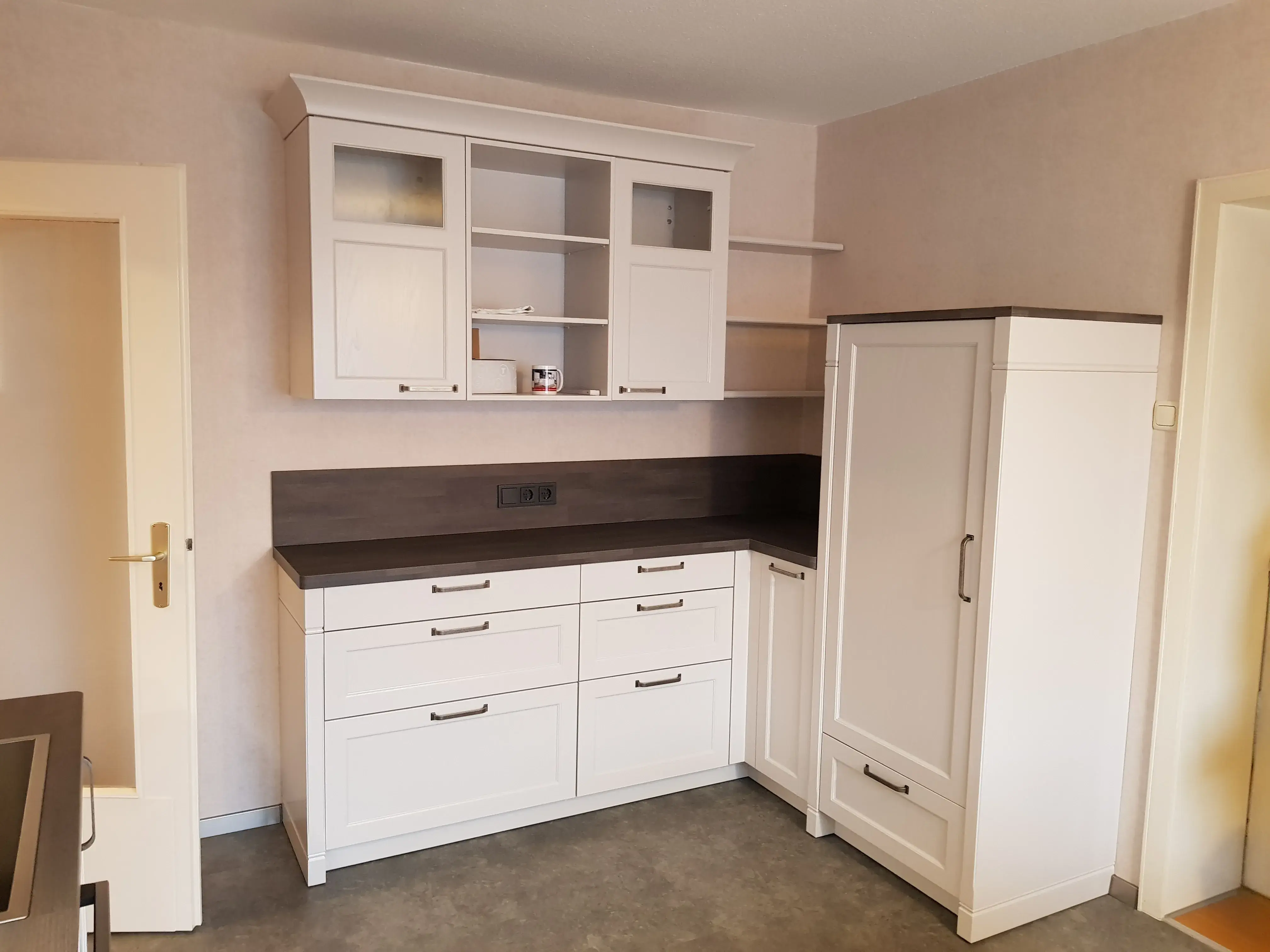 Weiße Küchenschränke mit dunkler Arbeitsplatte vor beiger Wand in einer leeren Küche.