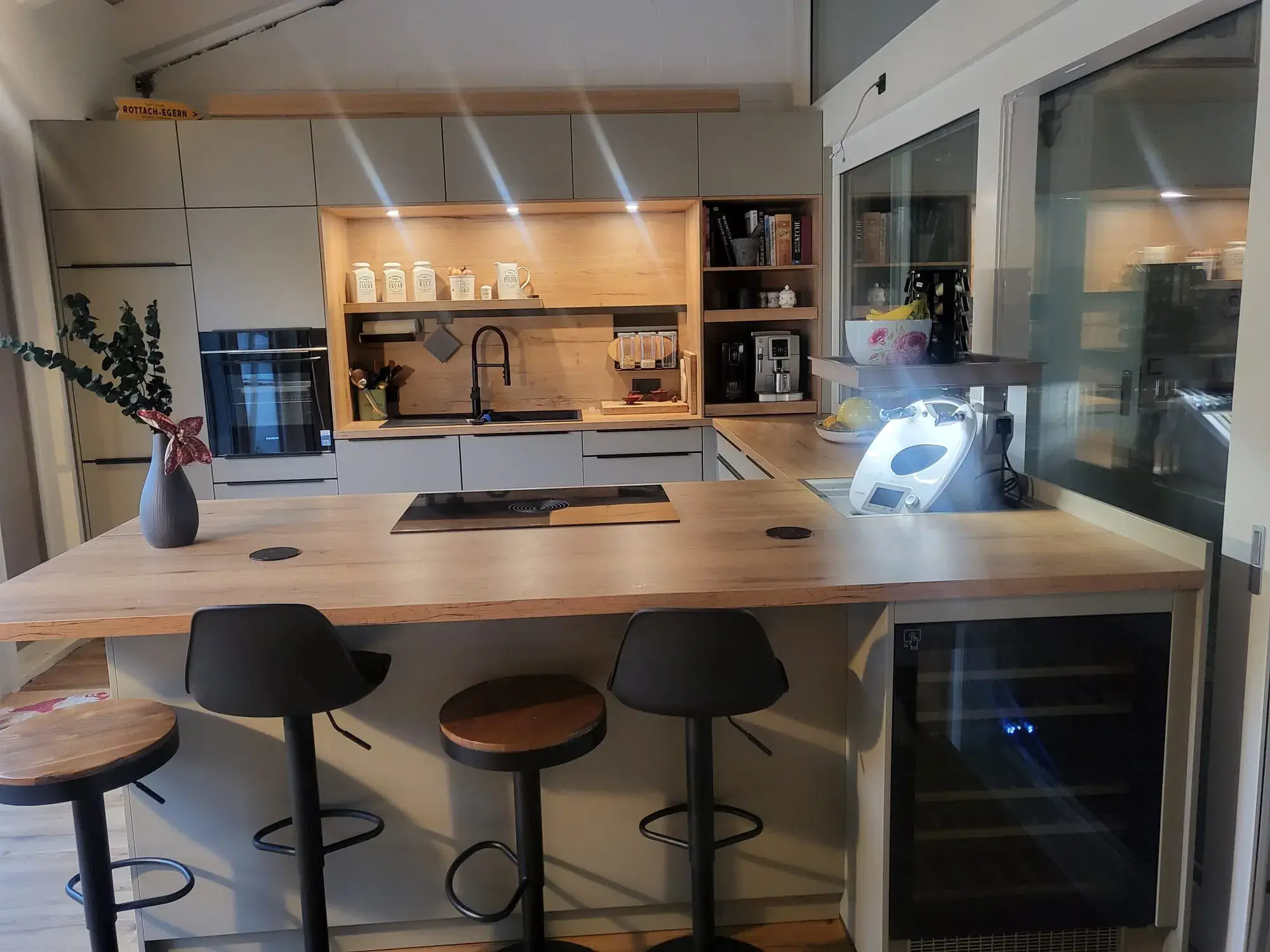 Moderne Küche mit Kochinsel, Holztheke und drei Barhockern. Helle, gemütliche Atmosphäre.