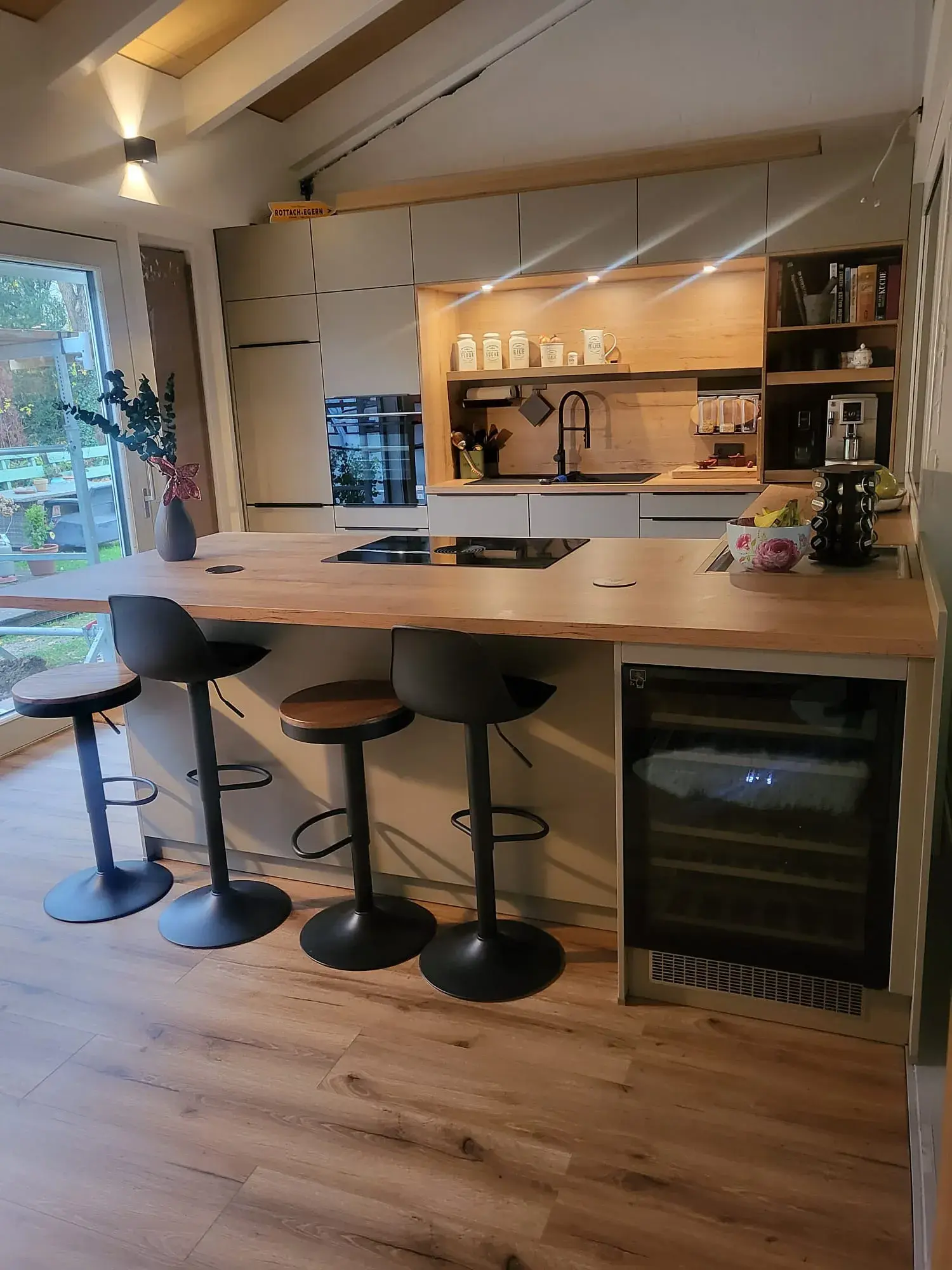 Moderne Küche mit Holztheke, vier Barhockern und großem Fenster, helle und gemütliche Atmosphäre.