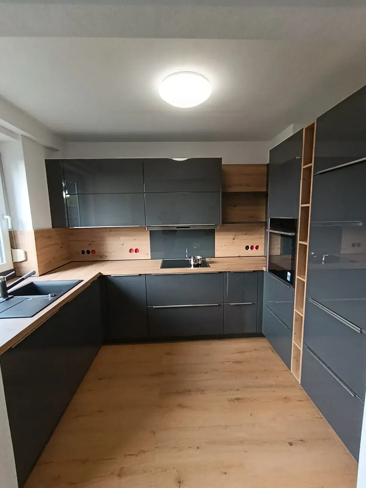 Moderne Küche mit grauen Schränken, Holzarbeitsplatte und hellem Holzboden.