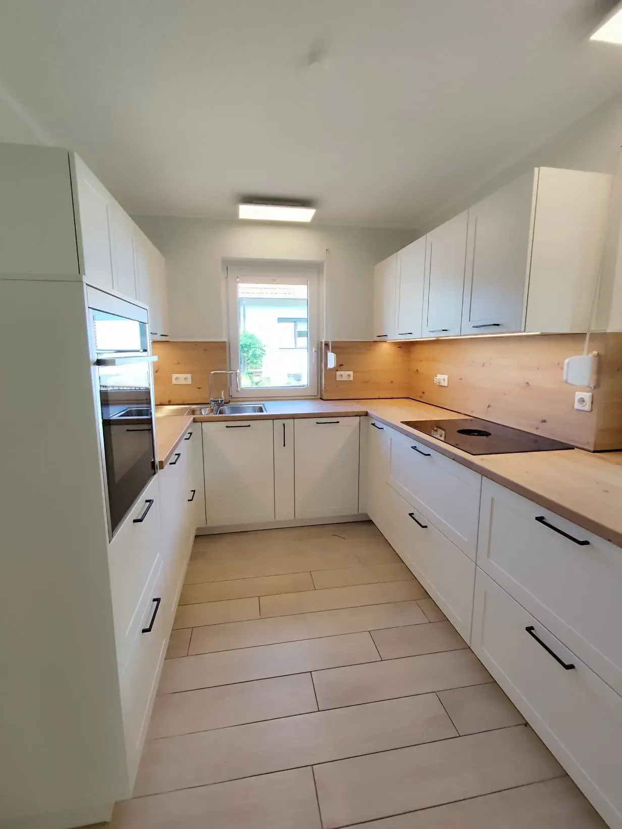 Helle, moderne Einbauküche mit weißen Schränken und Holzarbeitsplatte.