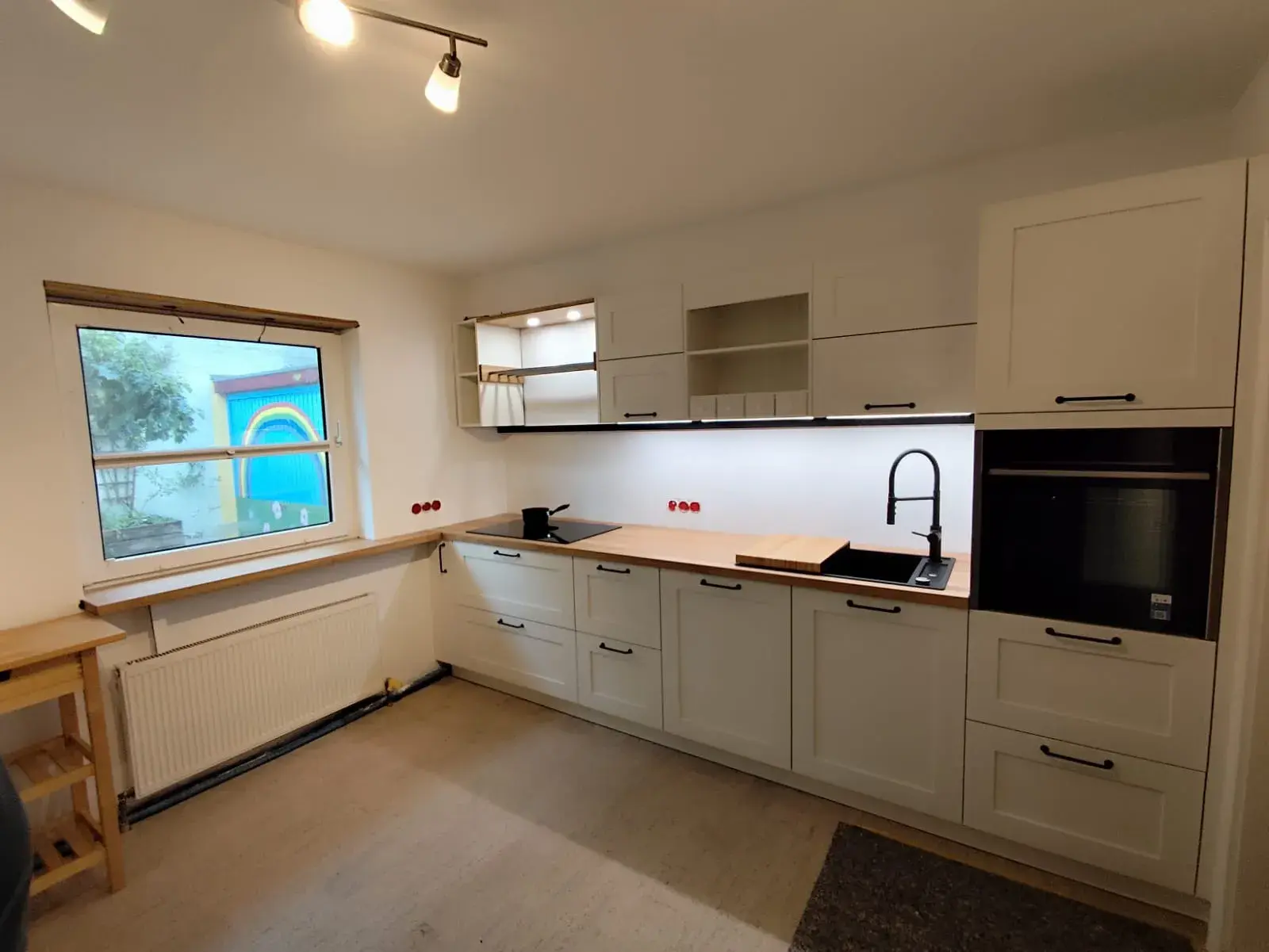 Moderne Küche mit weißen Schränken, Holzarbeitsplatte und großem Fenster