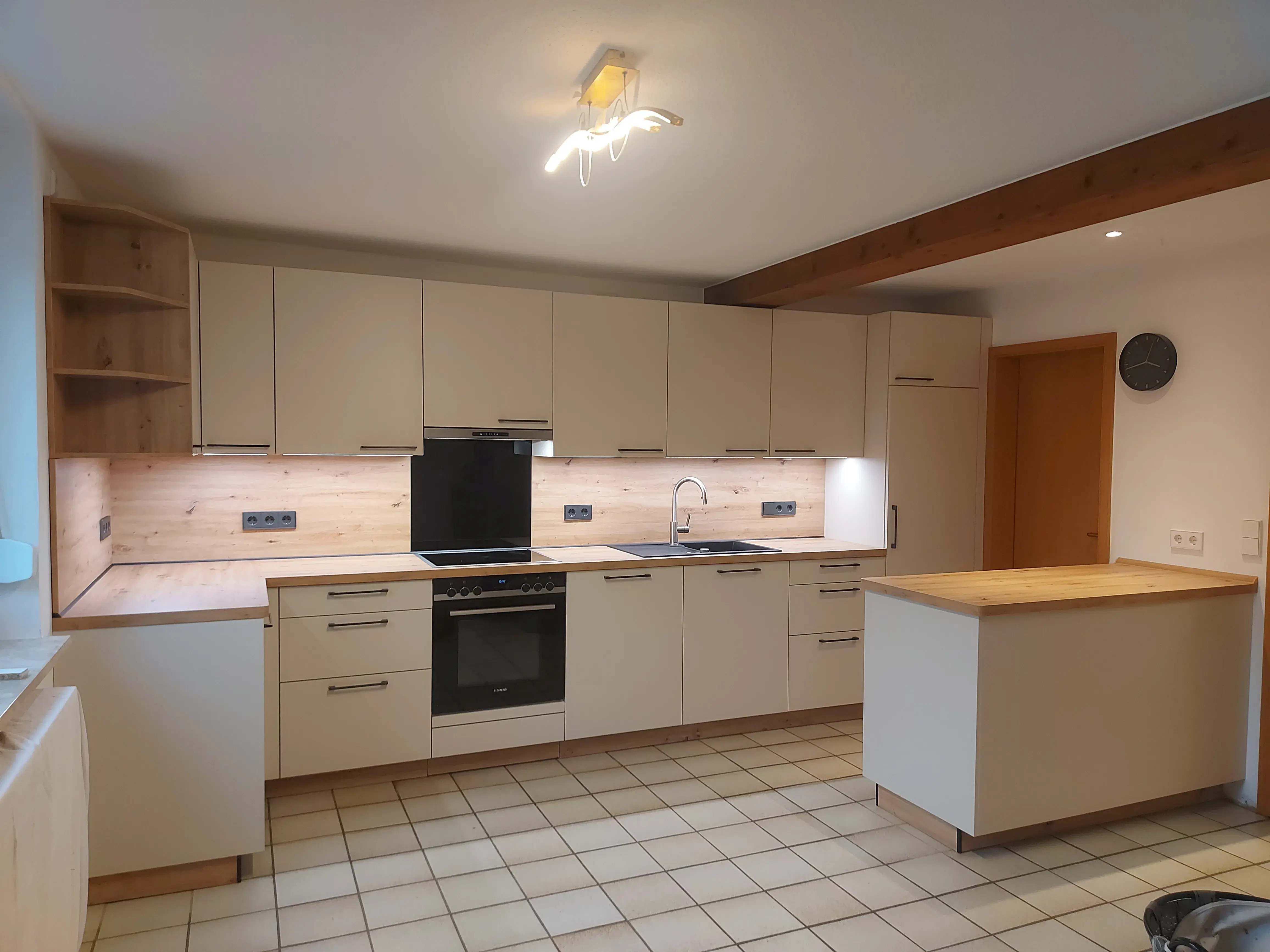 Moderne Einbauküche mit hellen Schränken, Ofen, Insel und Holzdetails.