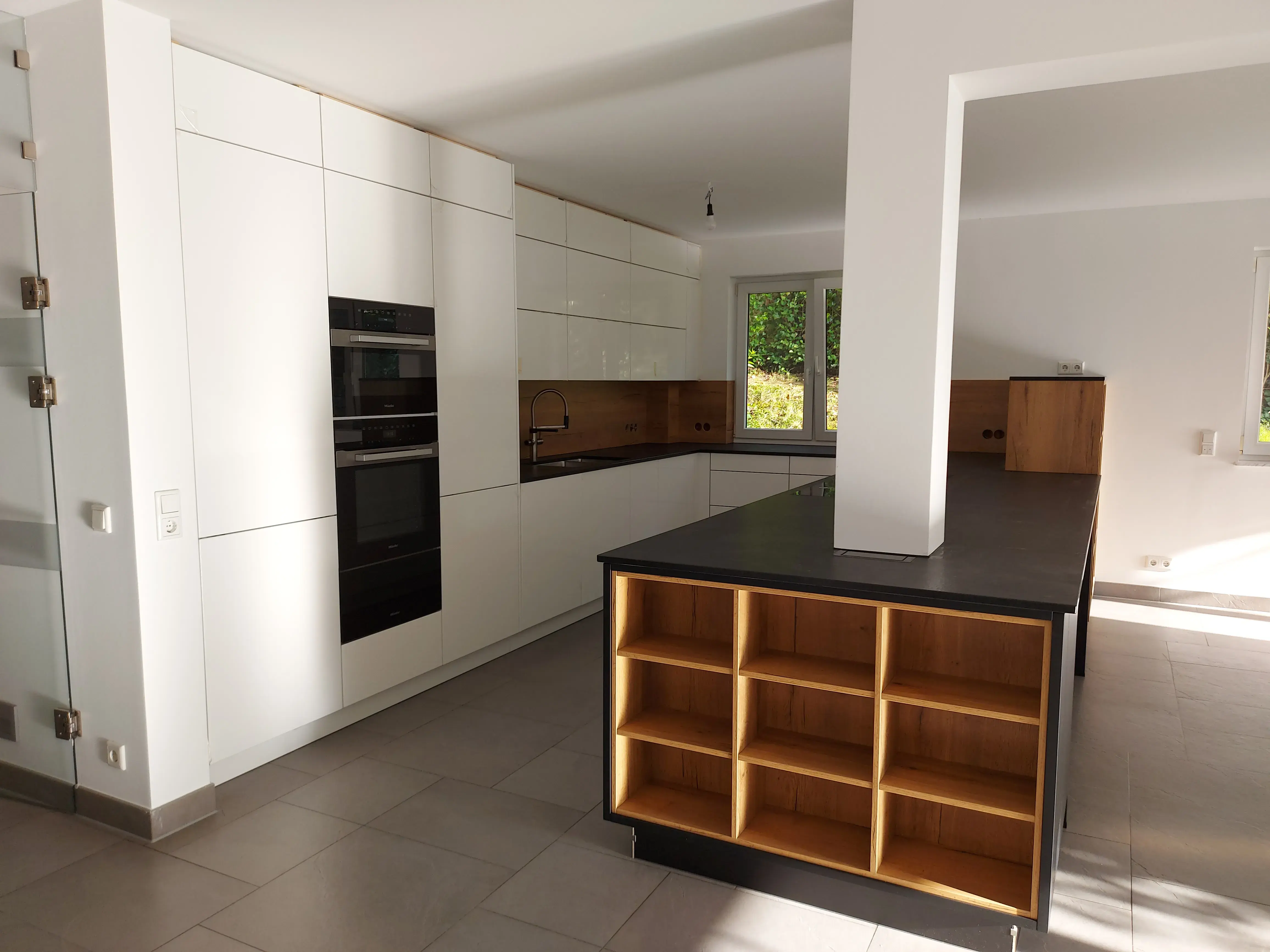 Moderne, helle Küche mit Kücheninsel, weißen Schränken und Holzregalen.