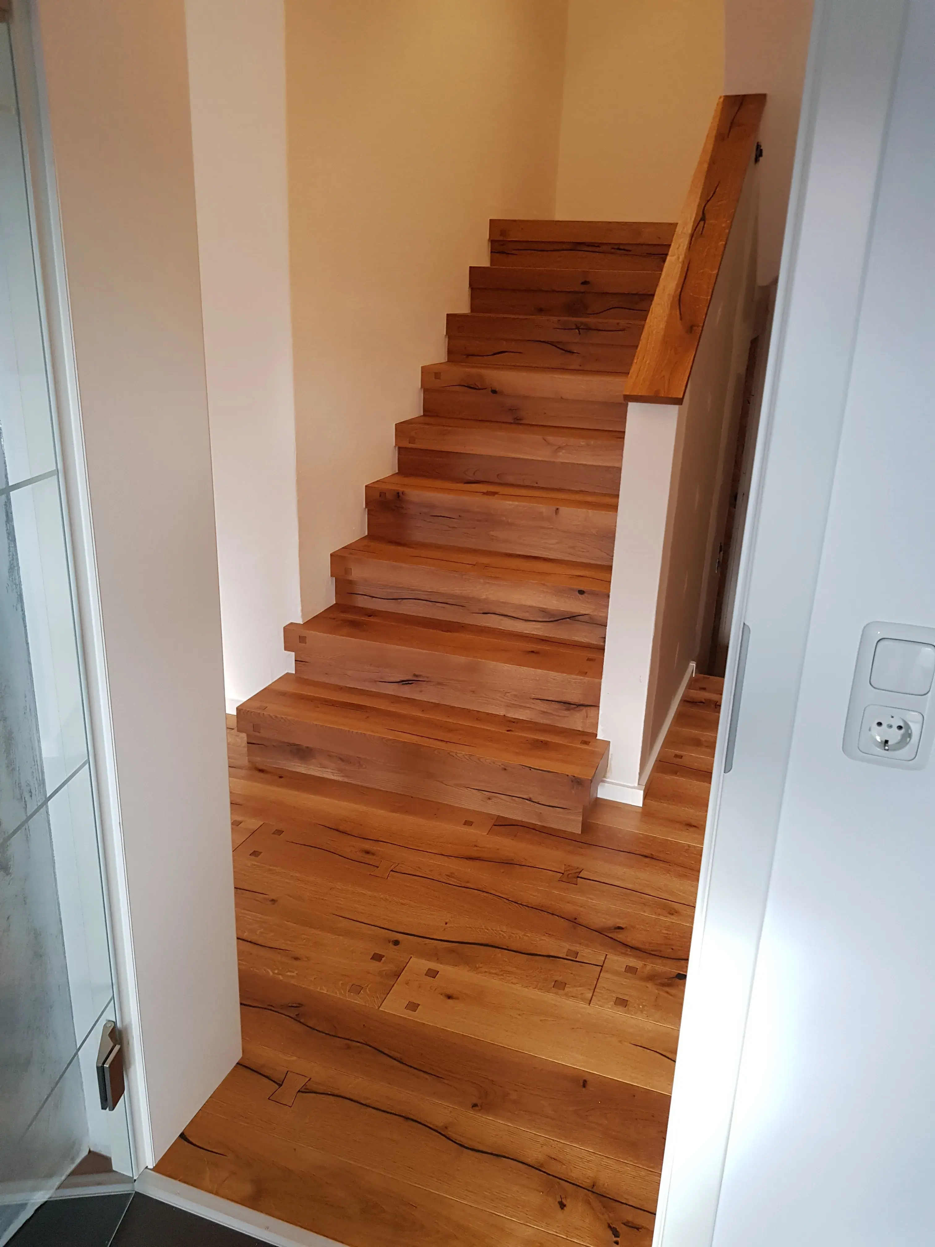 Holztreppe mit Geländer in einem hellen Flur, Holzboden und weiße Wände.