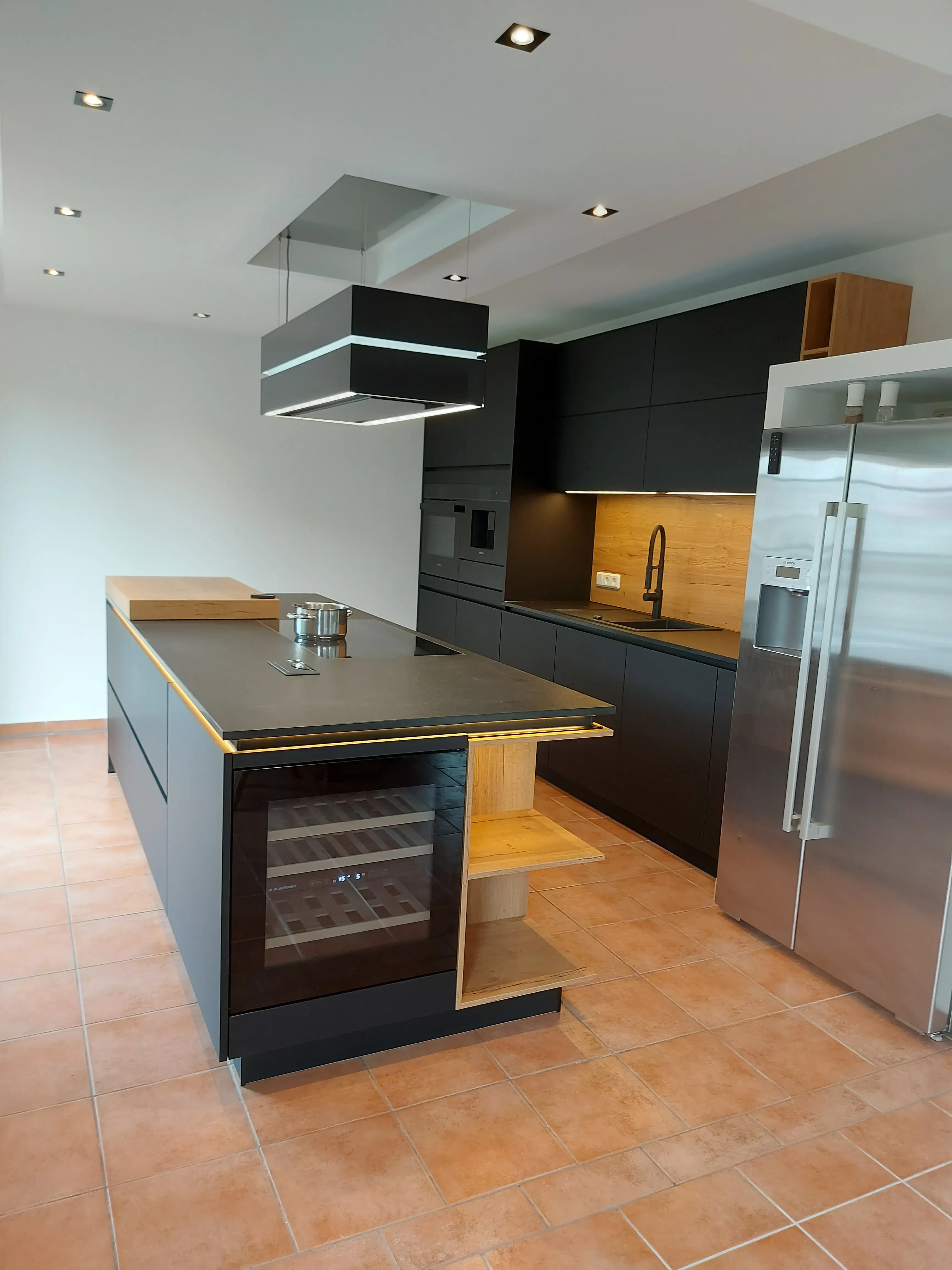 Moderne Küche mit Kochinsel, schwarzen Schränken und Edelstahl-Kühlschrank.