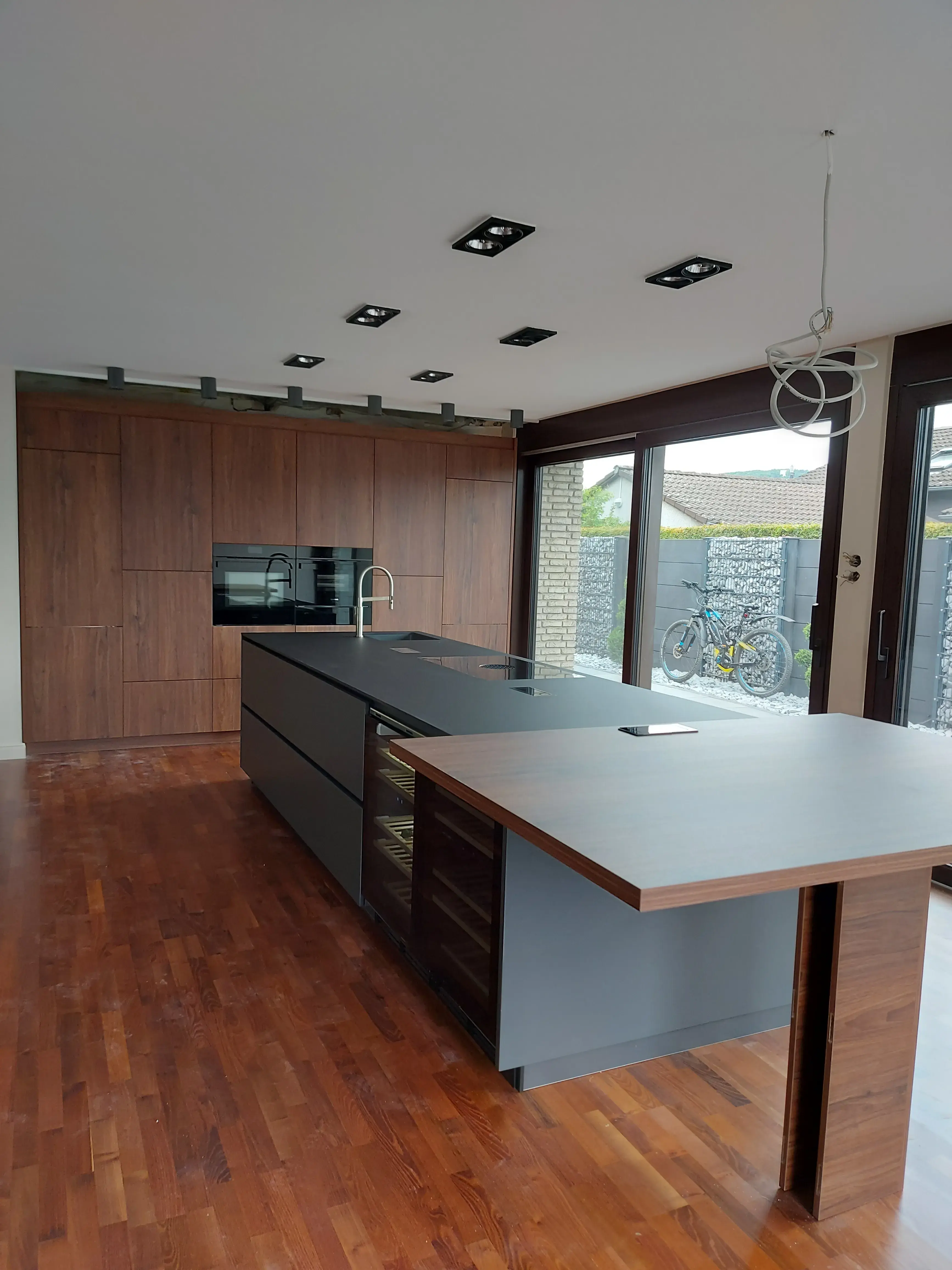 Moderne Küche mit Kochinsel, Holzboden und großen Fenstern.