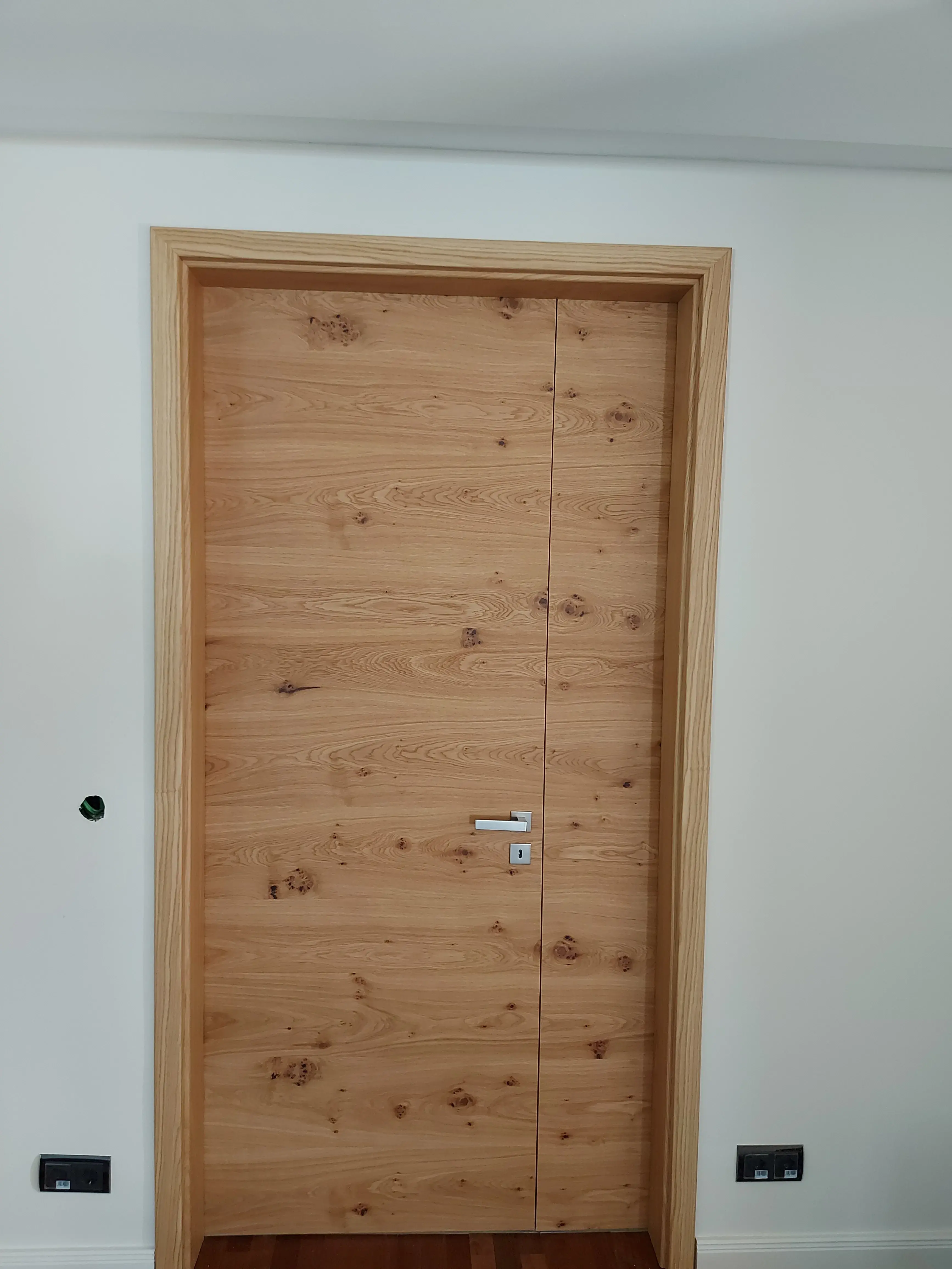 Geschlossene Holztür mit silberner Klinke in weißer Wand.